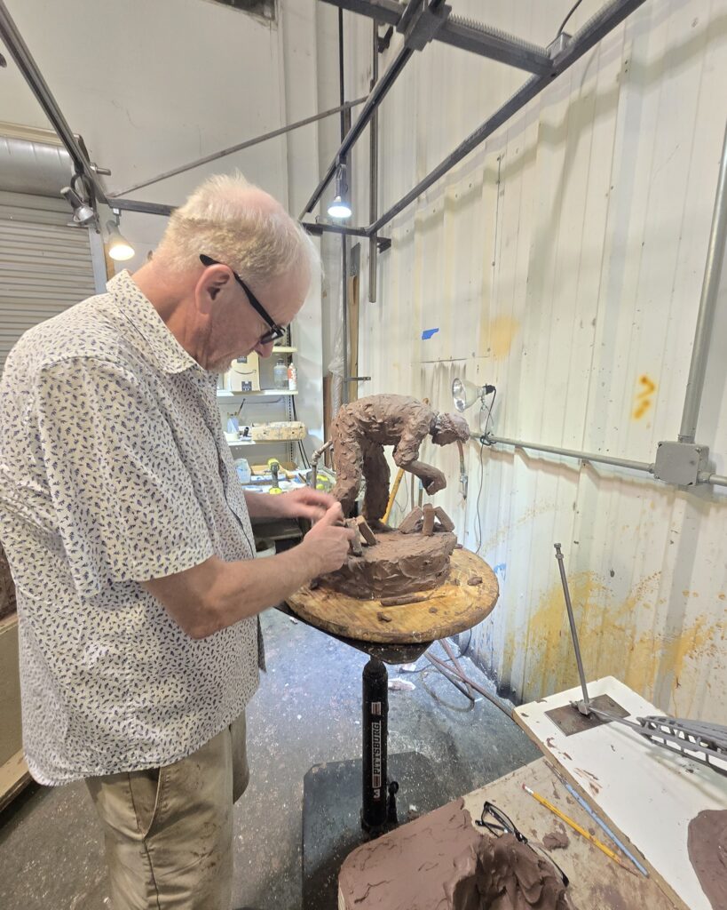 Handsome male artist sculpting detailed clay figure in studio.